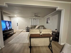 Un salon comprenant un téléviseur, un ventilateur de plafond, un tapis à motifs et un canapé.