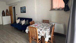 Un espacio habitable compacto con una mesa de comedor, sofá azul y una ventana pequeña con cortinas.