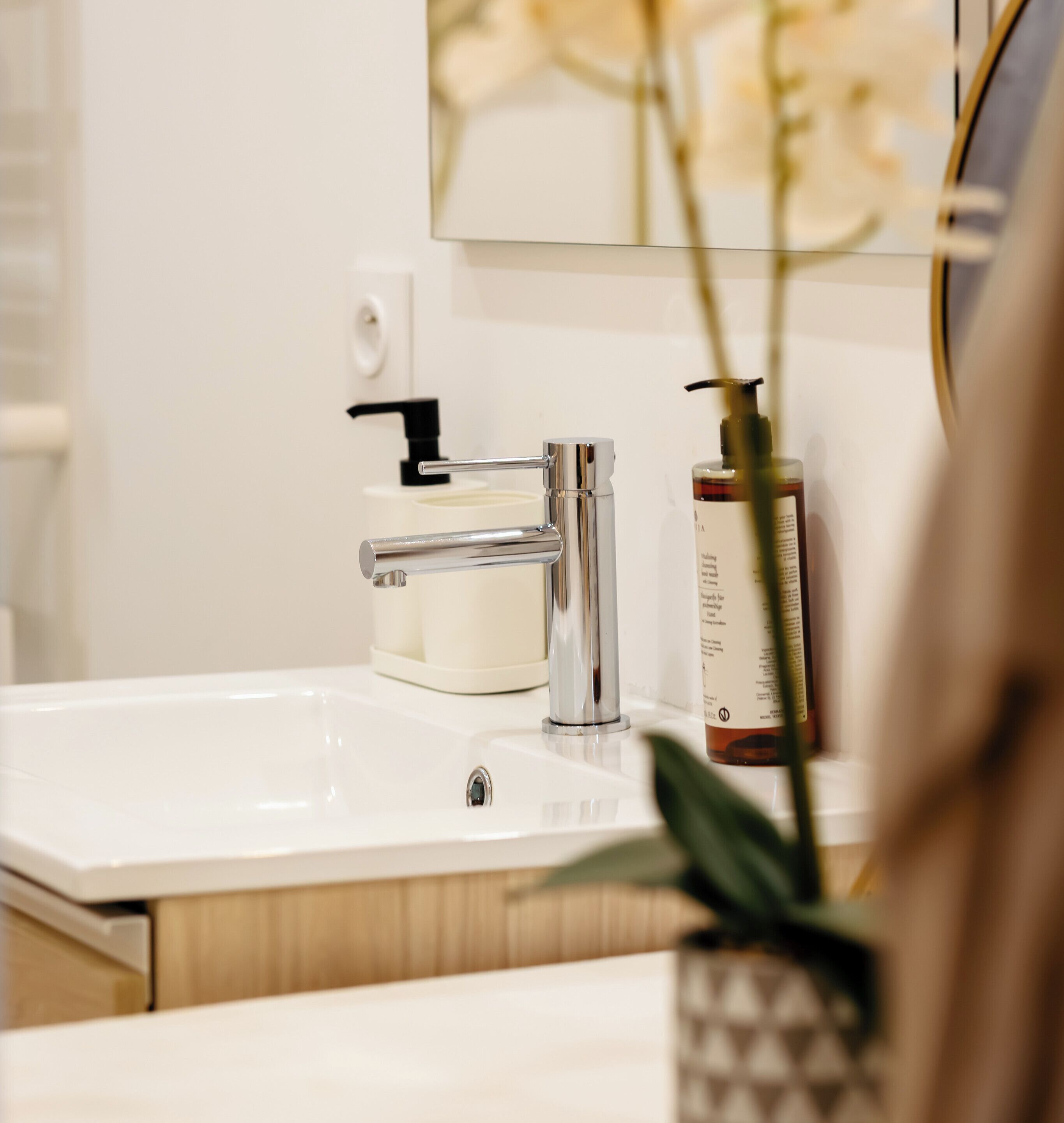 Un lavabo de salle de bain doté d’un robinet moderne, d’un distributeur de savon et d’un miroir au-dessus.