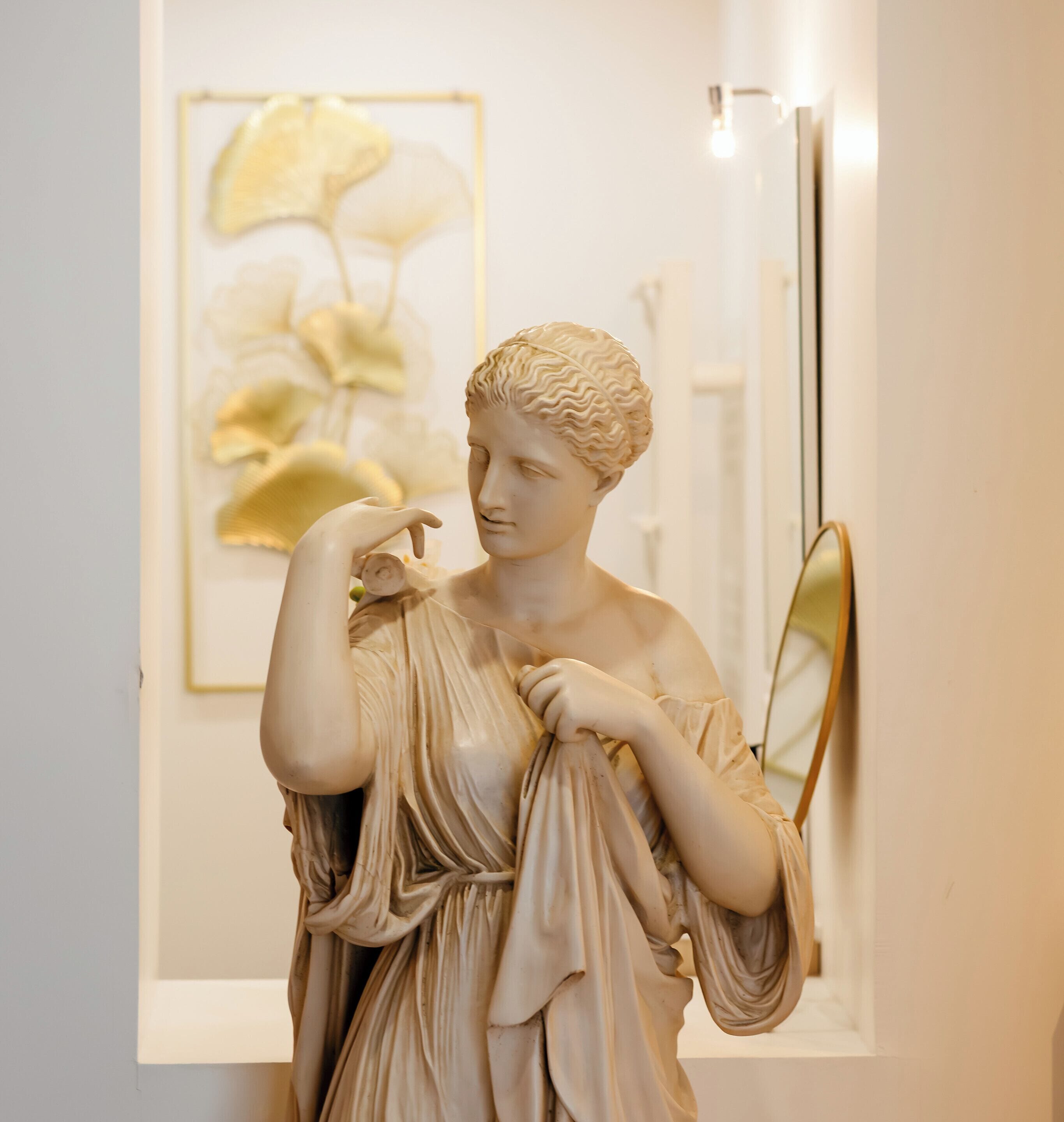 A marble statue of a woman in a classical pose, with a framed artwork and a mirror in the background.