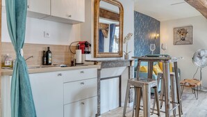 A modern kitchen with white cabinets, a marble countertop, a sink, and a coffee machine. There is a dining area with a table, chairs, and a fan.