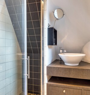 Ein Badezimmer mit einer Duschkabine aus Glas, einem weißen Waschbecken mit modernem Wasserhahn und einem kleinen Spiegel an der Wand.