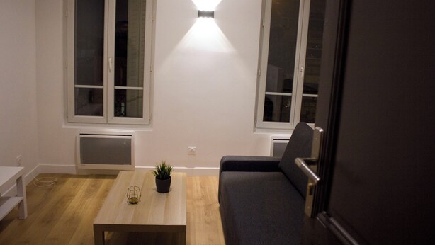 Una sala de estar pequeña y moderna con una mesa de centro de madera, un sofá negro y una planta en maceta.