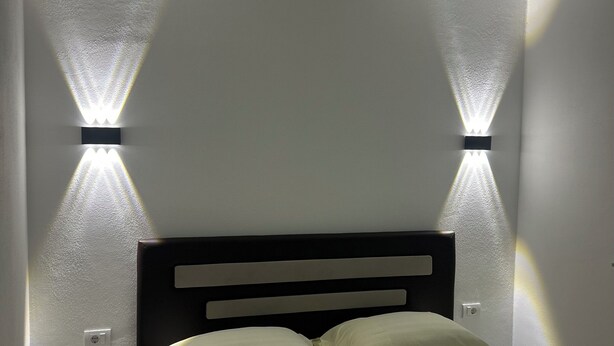 A bedroom with a bed, a headboard, and two wall-mounted light fixtures. - A family owned house (Ulcinj)