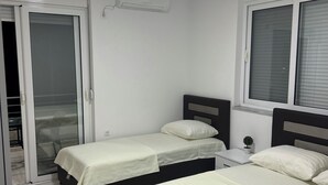 A bedroom with two beds, a small bedside table with a lamp, and a window with blinds. - A family owned house (Ulcinj)
