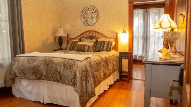 A neatly arranged bedroom with a bed, bedside lamps, a wall clock, and a window with curtains.