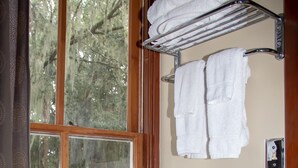 A bathroom with a toilet, a window with a view of trees, and a towel rack with towels.