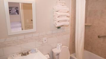 A bathroom with a sink, toilet, and shower. There are towels stacked on the wall.