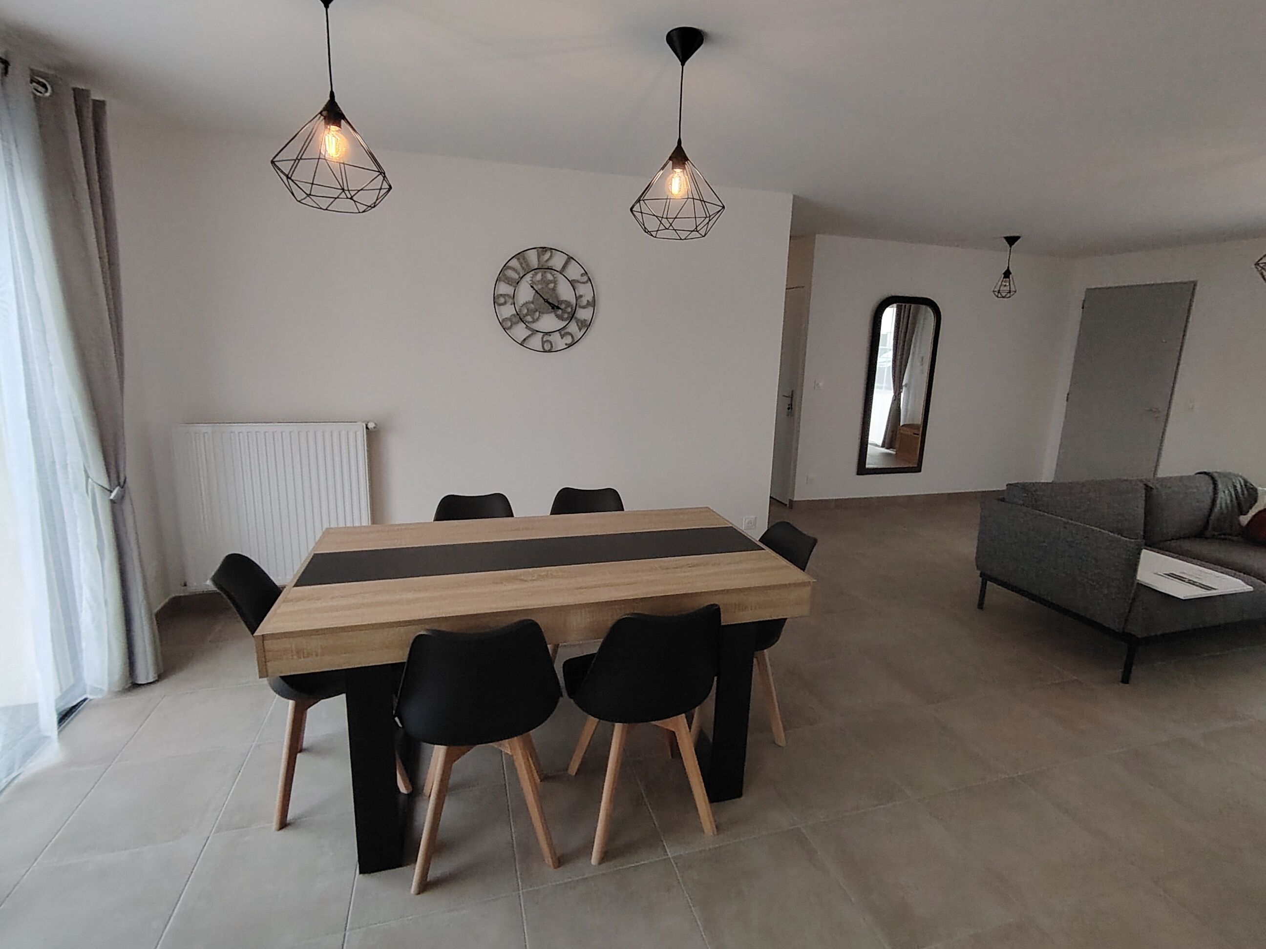 A modern living room with a wooden dining table, black chairs, and two pendant lights.