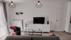 Una sala de estar moderna con un sofá, una mesa de centro de vidrio, un televisor de pantalla plana y decoración en la pared.