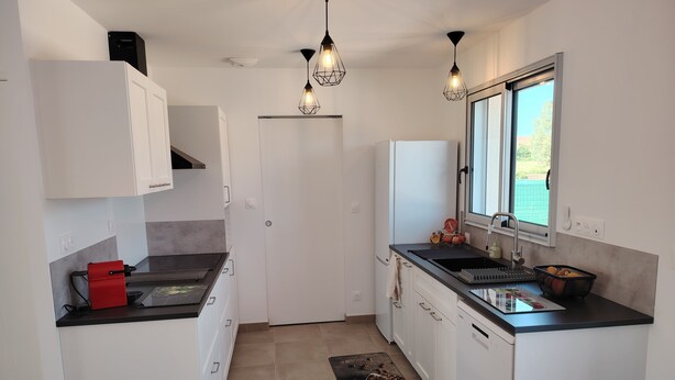 Una cocina moderna con armarios blancos, encimera negra, electrodoméstico rojo y ventana que proporciona luz natural.