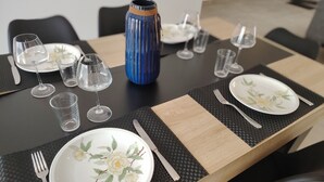 Una mesa de comedor puesta con platos, cubiertos, vasos y un jarrón decorativo.
