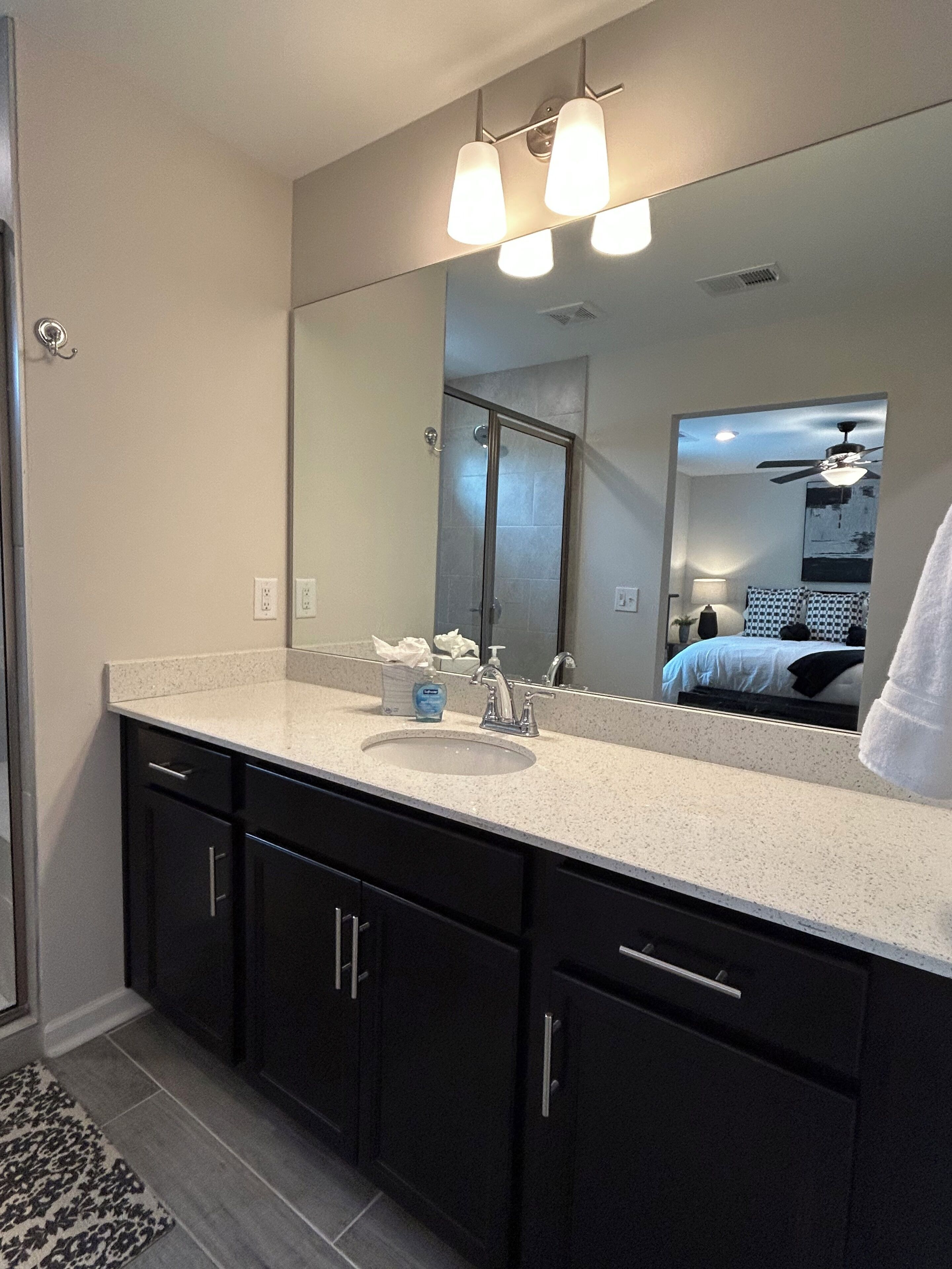 A modern bathroom with a large mirror, a sink, and dark cabinetry.