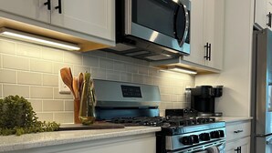 Una cocina moderna con armarios blancos, electrodomésticos de acero inoxidable y un microondas sobre la estufa.