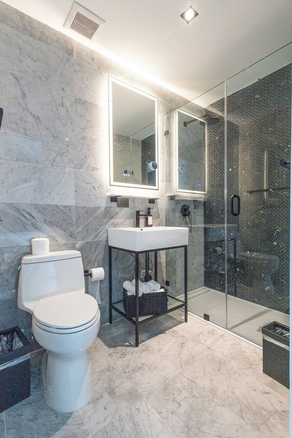 Un baño moderno con inodoro, lavamanos y ducha con mampara de vidrio.
