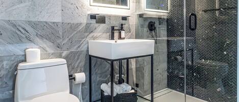 Un baño moderno con inodoro, lavamanos con marco negro y cabina de ducha con paredes de vidrio.
