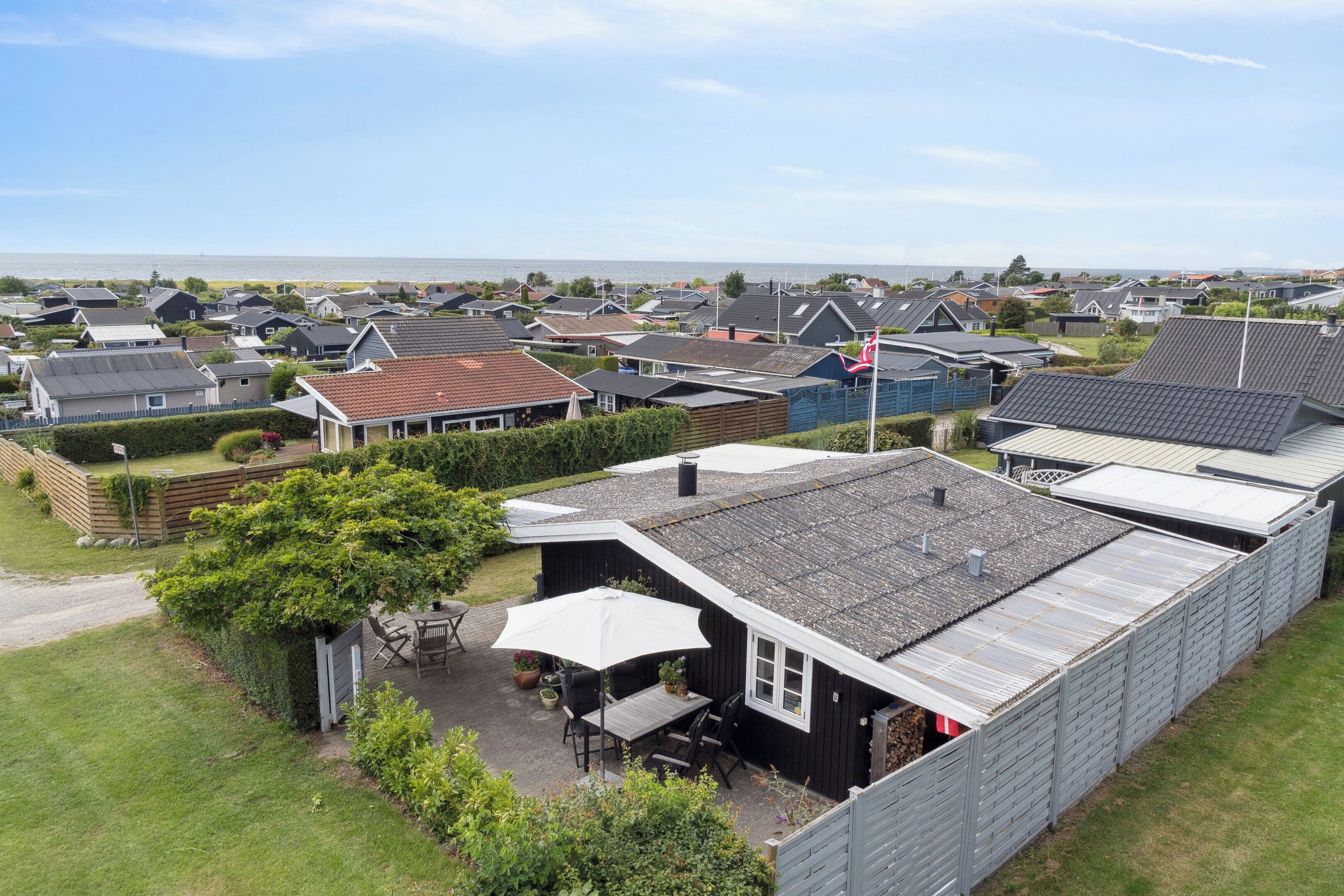 Ein Wohngebiet mit Häusern, einer Terrasse mit Gartenmöbeln und Blick aufs Meer.