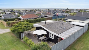 A residential area with houses, a patio with outdoor furniture, and a view of the sea.