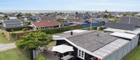 Ein Wohngebiet mit Häusern, einer Terrasse mit Gartenmöbeln und Blick aufs Meer.
