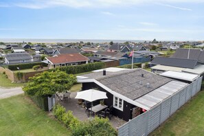 A residential area with houses, a patio with outdoor furniture, and a view of the sea.
