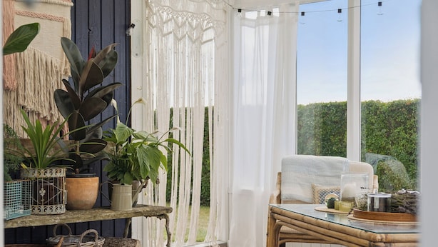 A cozy patio area with wicker furniture, potted plants, and a view of greenery.