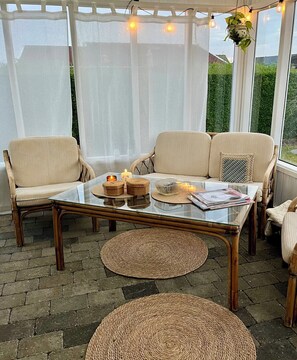 A cozy outdoor seating area with wicker chairs, a glass table, and a hanging plant.