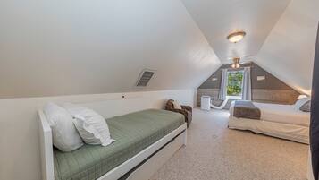 A small, sloped ceiling room with a bed, a chair, a heater, and a window with curtains.