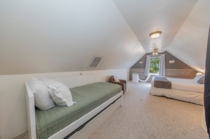 Habitación pequeña con techo inclinado, una cama, una silla, un calefactor y una ventana con cortinas.