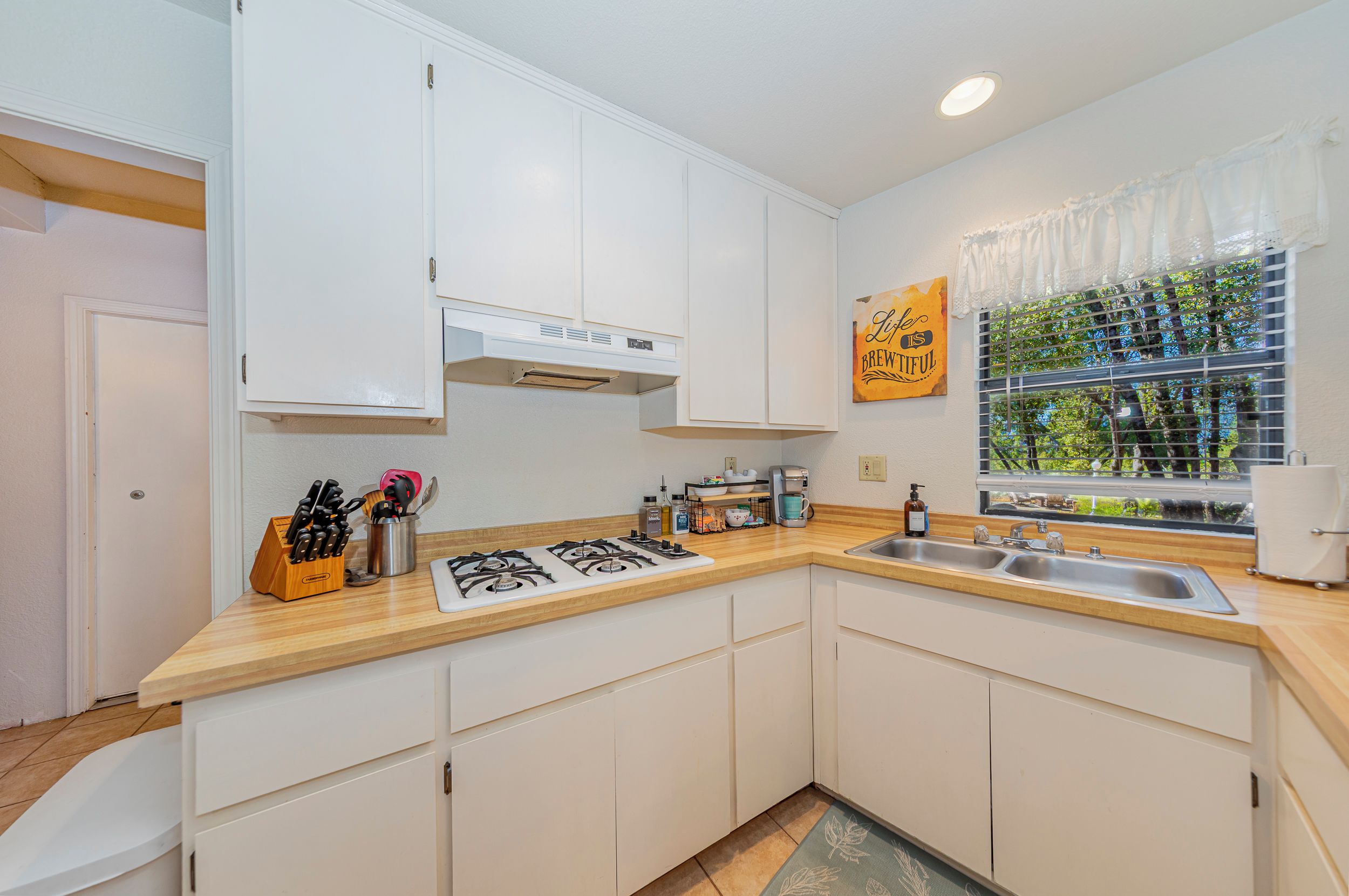A modern kitchen with white cabinets, a gas stove, a sink, and a window with a view of greenery.