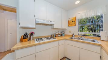 A modern kitchen with white cabinets, a gas stove, a sink, and a window with a view of greenery.