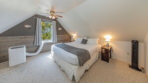Une chambre avec un plafond en pente, un lit avec une literie blanche, un radiateur et une fenêtre avec des rideaux.