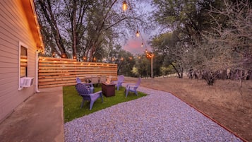 An outdoor patio area with a fire pit, seating, and string lights.