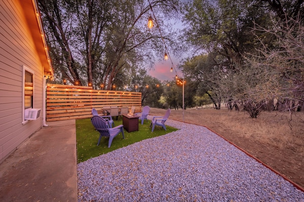 An outdoor patio area with a fire pit, seating, and string lights.