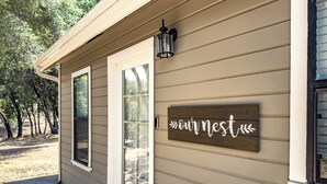 A house with a wooden sign reading "our nest" on the exterior wall, a front door, and a small porch area.