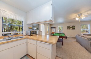 A modern kitchen with a built-in microwave, a sink, and a dining area with a pool table. - Yosemite Deer Cottage 1 Bed:1 Bath with Kitchenette (Oakhurst)