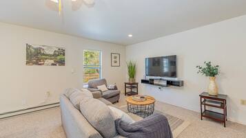 A living room with a sofa, a TV, a plant, and artwork on the walls.