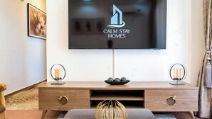Ein modernes Wohnzimmer mit einem flachbildfernseher an der Wand, einem hölzernen Konsolentisch mit Schubladen und zwei dekorativen Lampen.