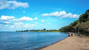 Ein Strand mit blauem Himmel und ruhigem Wasser, umgeben von viel Grün.