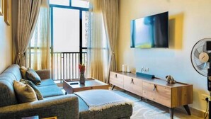 Ein Wohnzimmer mit einer Couch, einem an der Wand montierten Fernseher, einem Holzschrank und einem Ventilator.