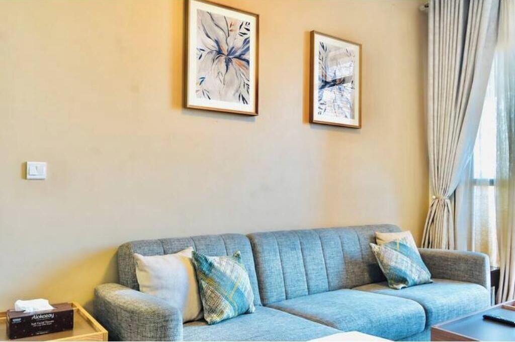 A living room with a grey sofa, two framed abstract paintings, and a window with curtains.