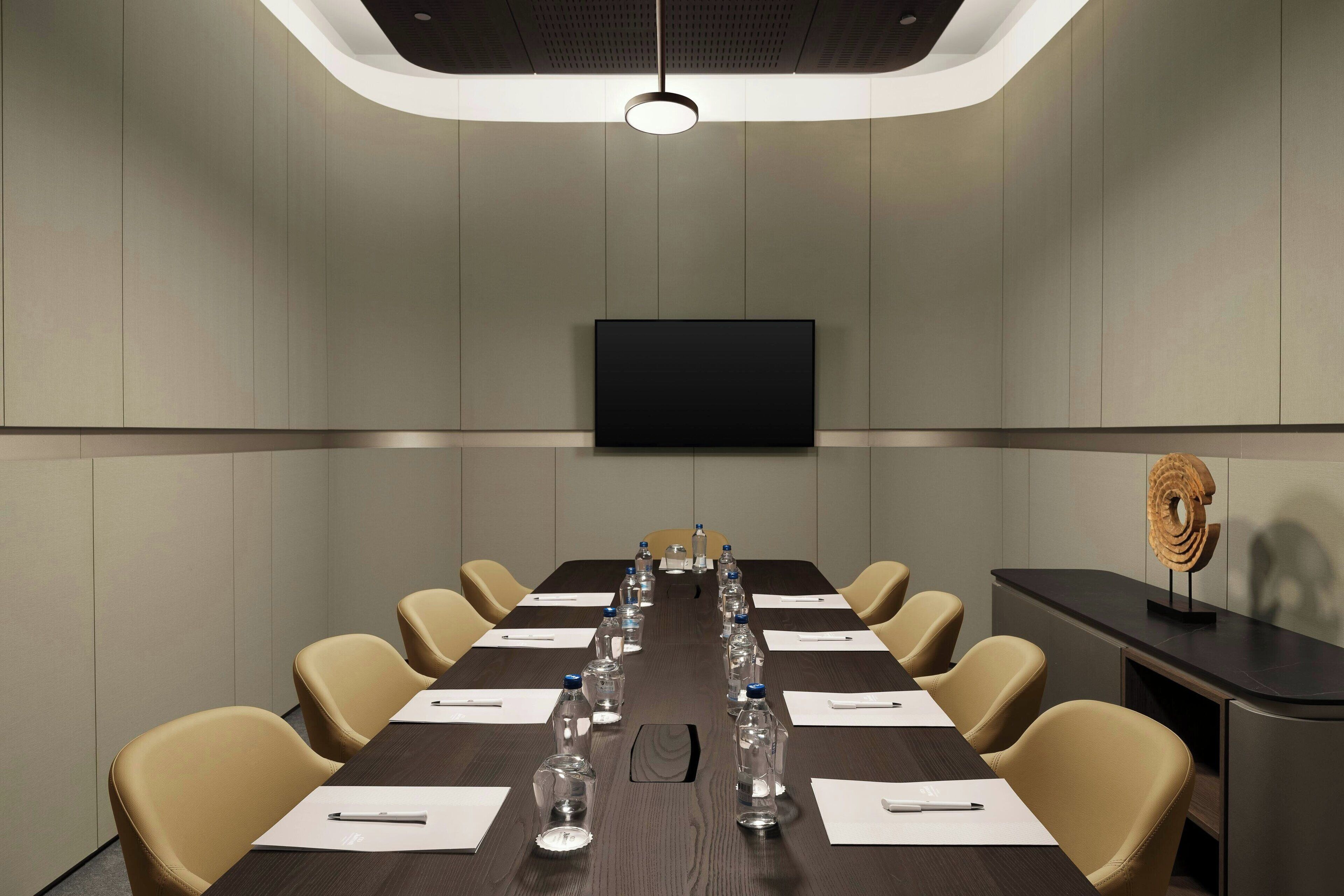 Un salón de conferencias con una mesa larga, sillas, botellas de agua y un televisor de pantalla plana en la pared.