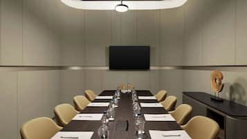 Un salón de conferencias con una mesa larga, sillas, botellas de agua y un televisor de pantalla plana en la pared.