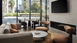 A modern living room with a sofa, chairs, a coffee table, and a fireplace. A TV is mounted on the wall, and there is a view of buildings and trees outside. - Marriott Executive Apartments Antalya (Antalya)