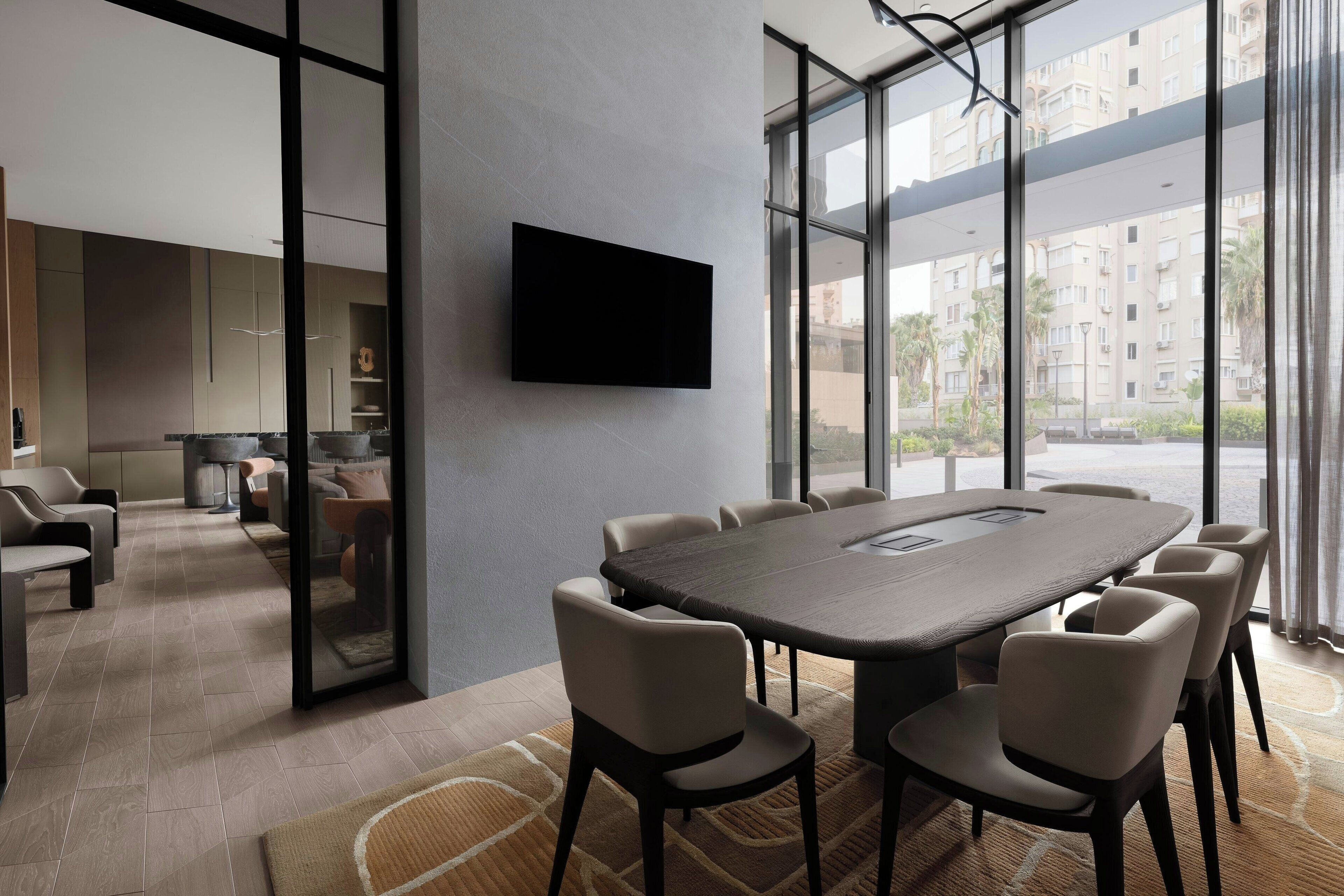 Un salón de conferencias moderno con una mesa grande y sillas, un televisor de pantalla plana en la pared y ventanas amplias con vistas a la ciudad.