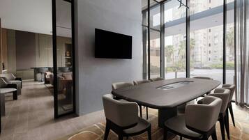 Un salón de conferencias moderno con una mesa grande y sillas, un televisor de pantalla plana en la pared y ventanas amplias con vistas a la ciudad.