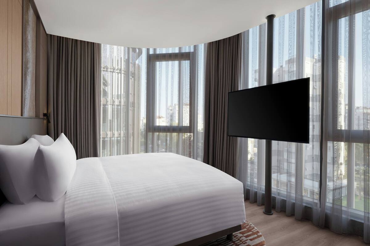 Une chambre d’hôtel moderne dotée d’un grand lit, d’une télévision à écran plat et de grandes fenêtres avec des rideaux.