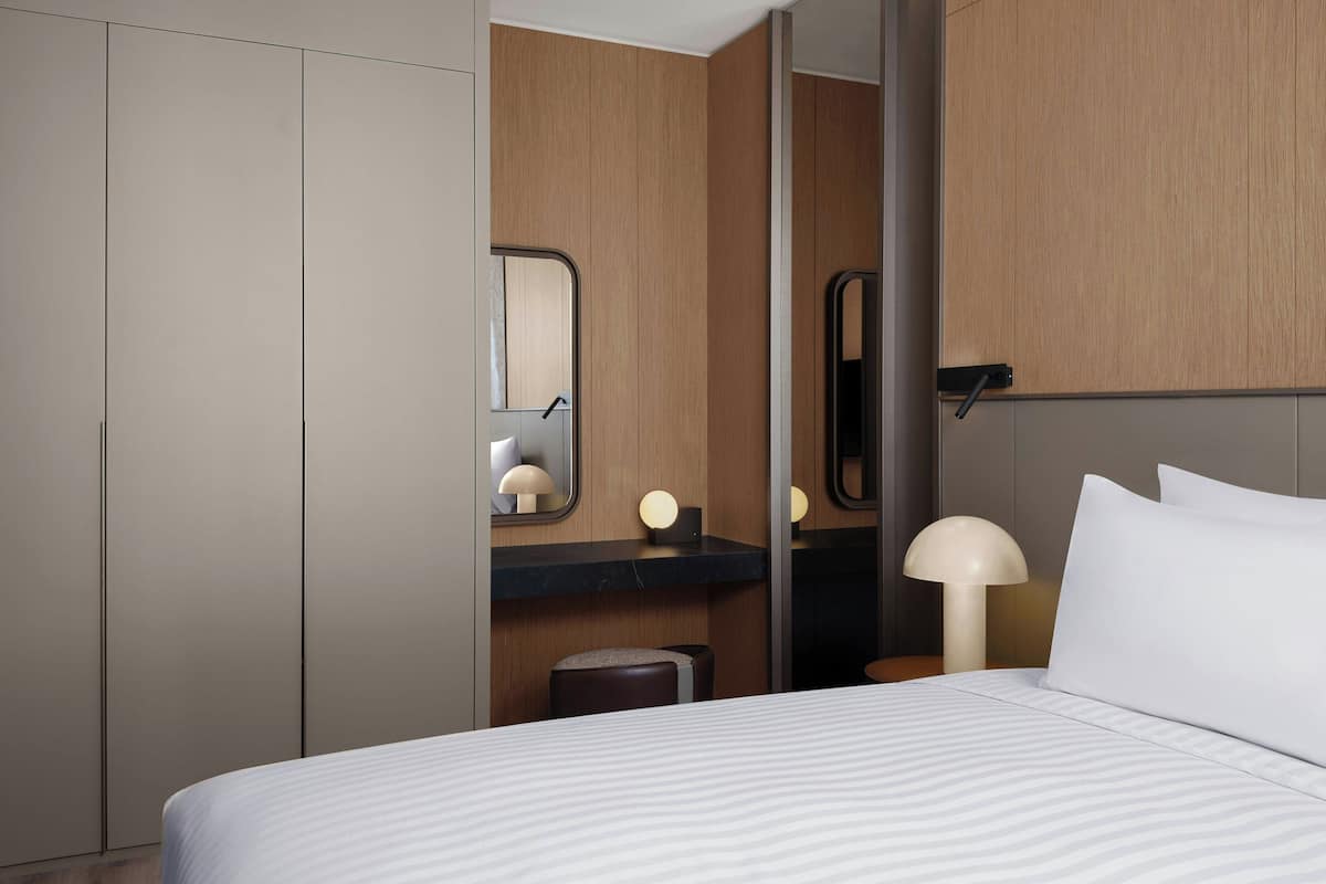 Une chambre d’hôtel comprenant un lit, une table de chevet, un miroir et une armoire.