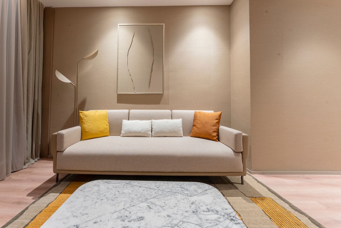 A modern living room with a beige sofa, a marble-patterned rug, and a minimalist wall art piece.