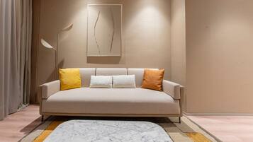 A modern living room with a beige sofa, a marble-patterned rug, and a minimalist wall art piece.
