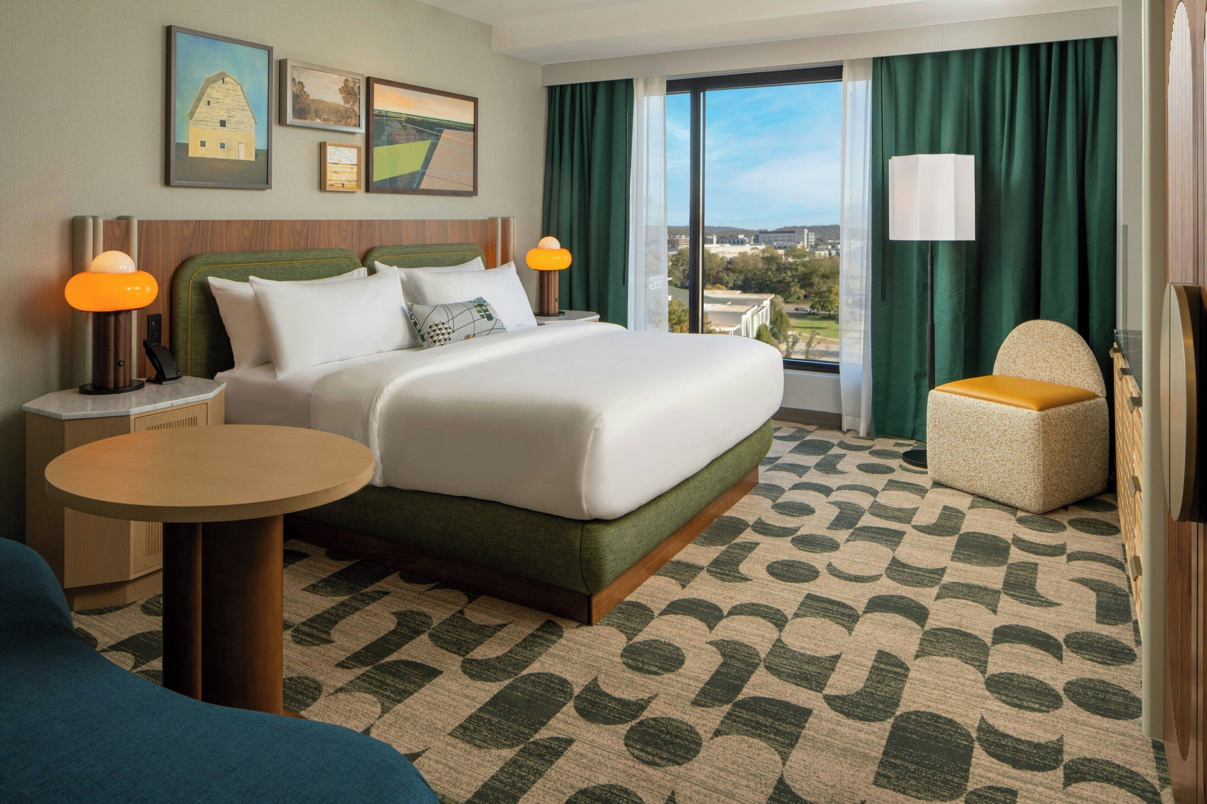A hotel room with a large bed, a round table, a chair, and a view of the outdoors.
